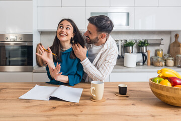 Young engaged couple standing together in their modern kitchen, writing wedding guest list and...