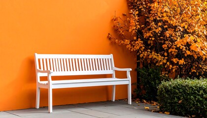 White Park Bench Against Orange Wall with Autumn Foliage, and Serene Outdoor Scene.