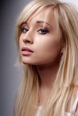 Naklejka premium Close-up portrait of a blonde woman showcasing her natural beauty with soft features and elegant makeup, offering a serene and confident expression in front of a neutral background.