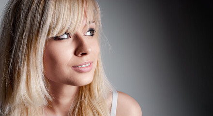 A blonde woman gazing thoughtfully to the side, against a plain neutral backdrop. The image...