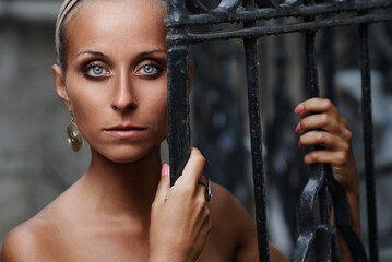 Close-up portrait of an elegant woman holding an ornate iron gate, conveying confidence and...