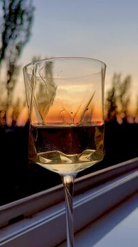 Close-up of a wine glass capturing the warm hues of a fading sunset, with delicate water droplets creating beautiful reflections.