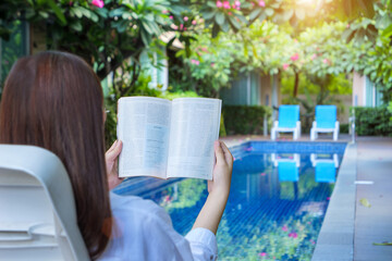 summer holidays, woman reading book near swimming pool with frangipani trees planted around it at hotel on travel holidays vacation weekend, wellness lifestyle concept.