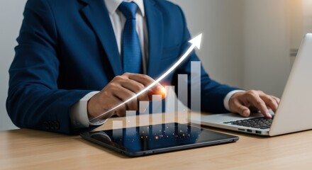 Businessman works on laptop and tablet with rising graph overlay representing business growth