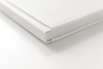 corner of book in white leather cover on white table. binding for photo album