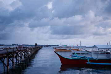 Wooden Dock Over Calm Ocean with Boats Under Majestic Cloudy Sky