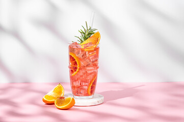 Blood orange cocktail with ice and rosemary on a marble stand on a pink white background