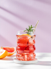 Refreshing mocktail with grapefruit, rosemary and ice in a glass on a white pink background