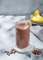 Chocolate smoothie with banana and coffee in a glass on a light  background with morning shadow.