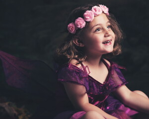 A young girl dressed as a fairy smiles while looking up.