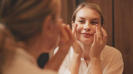 Young adult happy woman applying cream on face around the eyes, lightening under eye healthy skin care moisturizing nutrition white gel. girl looking in mirror reflection using anti-aging cosmetics - Powered by Adobe