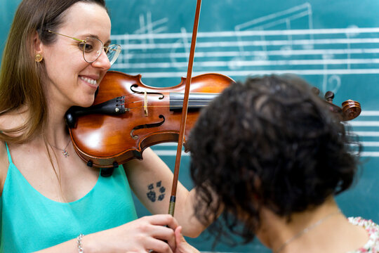 Music teacher helping student playing violin during lesson - Powered by Adobe