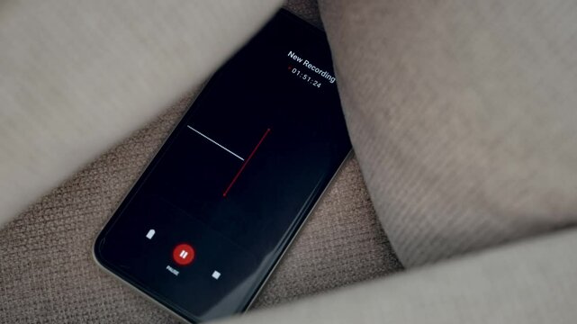 Smart phone with audio recording app hidden between pillows in sofa or couch. Close up mobile application secretly capturing and grabbing sound of conversation. Eavesdropping and wiretapping operation