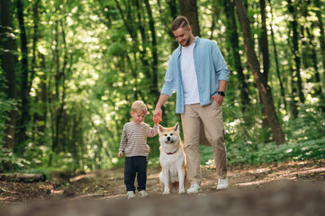 Fototapeta premium Front view, having a walk. Father with son and dog are in the forest