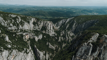 Panoramic aerial view of Lazar Canyon in eastern Serbia, revealing steep limestone cliffs and dramatic green-carpeted ridges stretching into distance. The vast landscape emphasizes the wild beauty