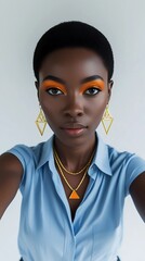 Portrait of an African girl looking at the camera, she has short black hair, orange eye shadow, heavy jewelry, and she is wearing a light blue shirt.