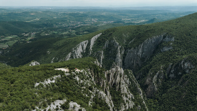 Aerial view of a small red-roofed shelter perched on a rocky plateau near Lazar Canyon, surrounded by dense forest and dramatic mountain ridges. Wooden gazebo on the edge of a cliff