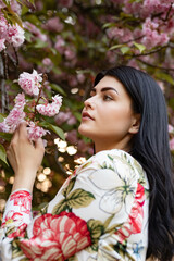 Fototapeta premium A serene image of a woman observing pink cherry blossoms, embodying spring's vitality and natural beauty. The soft light and floral surroundings create a calm, fresh, and contemplative atmosphere.