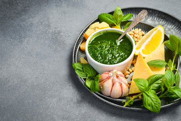 A bowl of homemade pesto sauce. Ingredients for making the sauce: basil, parmesan, nuts, lemon and...
