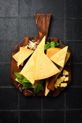 Cheese. Sliced ​​hard aged cheese and basil on a wooden cutting board.