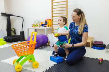 Boy patient undergoing physical rehabilitation stands confidently wearing special orthopedic shoes and compression suit in rehab clinic with therapist