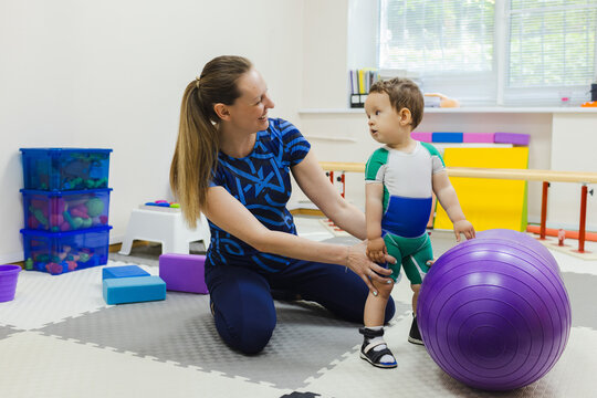 Dedicated therapist assists a young boy with movement disorders as she practices standing, enhancing her physical rehabilitation in rehab room