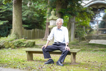 Obraz premium In rural Japan, a Japanese man in his late 70s takes a quiet rest at a countryside shrine surrounded by lush nature. Wearing a white shirt and hat, he sits calmly, enjoying the early summer air.