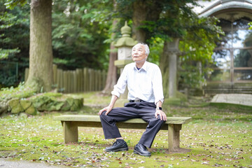 Obraz premium In rural Japan, a Japanese man in his late 70s takes a quiet rest at a countryside shrine surrounded by lush nature. Wearing a white shirt and hat, he sits calmly, enjoying the early summer air.