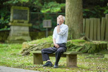 Obraz premium In rural Japan, a Japanese man in his late 70s takes a quiet rest at a countryside shrine surrounded by lush nature. Wearing a white shirt and hat, he sits calmly, enjoying the early summer air.