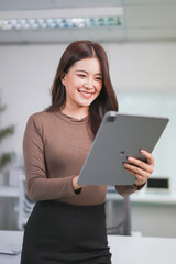 Young businesswoman is smiling while using a digital tablet in a modern office, showcasing the efficiency and connectivity of technology in the workplace