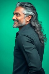 Naklejka premium Green solid background. An artistic and modern man captured in a studio. Fashionable men's wavy fringe haircut - midlife indian man with long hair. Creative of style for aging men.