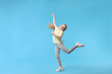 Obraz premium Cute little girl dancing on light blue background