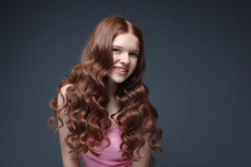 Fototapeta premium Portrait of smiling teenage girl with healthy wavy hair on dark grey background