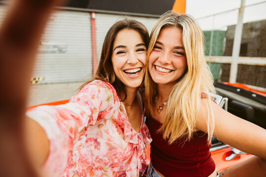 Two young women taking a selfie while leaning on convertible car