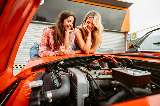 Two young women admiring engine of classic car during road trip