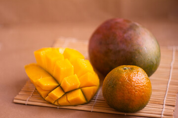 Freshly Sliced Mango and Whole Tangerine Displayed on Bamboo Mat
