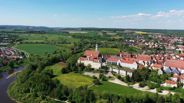 Luftaufnahme von Donauw&ouml;rth mit roten D&auml;chern, historischen Geb&auml;uden und einem markanten Turm, eingebettet in eine gr&uuml;ne Landschaft. Die Stadt bietet eine charmante Kulisse. 