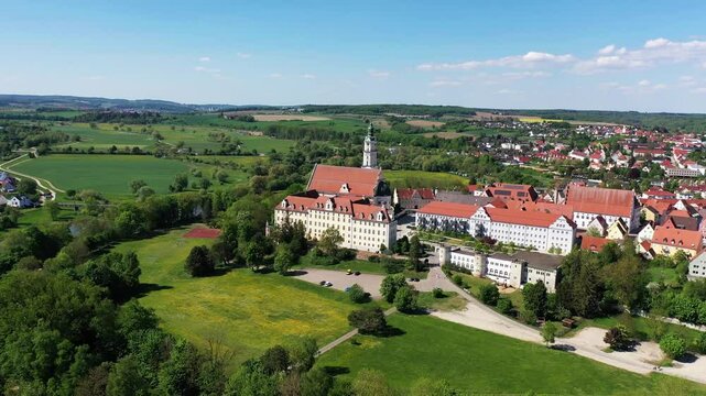 Luftaufnahme von Donauw&ouml;rth mit roten D&auml;chern, historischen Geb&auml;uden und einem markanten Turm, eingebettet in eine gr&uuml;ne Landschaft. Die Stadt bietet eine charmante Kulisse. 
