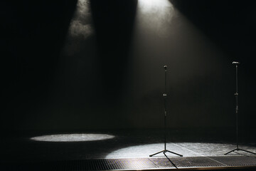 Dark stage with two microphone stands under dramatic spotlights, creating a moody and atmospheric...