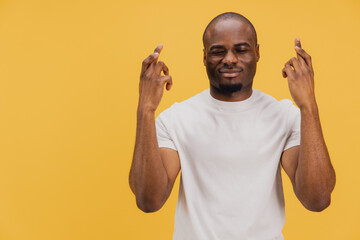 Young man crossing fingers hoping for good luck on yellow background