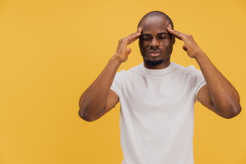 Young man suffering from headache touching temples on yellow background