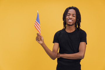 Young african american man holding United States flag on yellow background