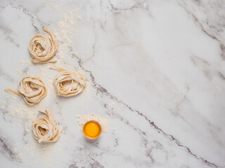 Rolled pasta over a marble surface with a raw egg. Flat lay with a bright background