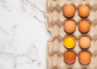 Egg box with an open egg on a white marble counter.