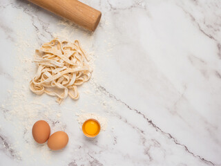 Fresh pasta over a kitchen counter with a rolling pin and some eggs