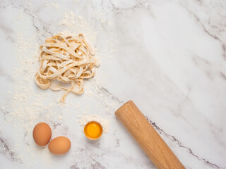 Fresh pasta over a kitchen counter with a rolling pin and some eggs