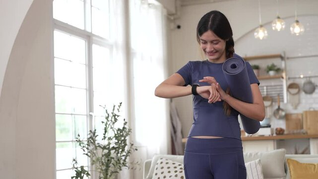 Fitness woman holding yoga mat and look at smartwatch checking heart rate, calories burned, tech in home gym, fitness, health tracking, self care, technology and healthy living, digital wellness
