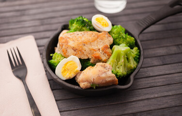 Chicken breast with broccoli and quail eggs in small cast iron skillet