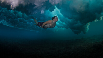 Man dives and swims underwater under the breaking wave