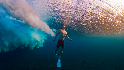 Man dives and swims underwater under the breaking wave